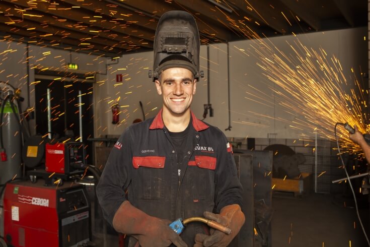 Lachende lasser met vonken in de werkplaats.
