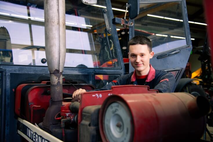 Monteur werkt aan motor van tractor in werkplaats.