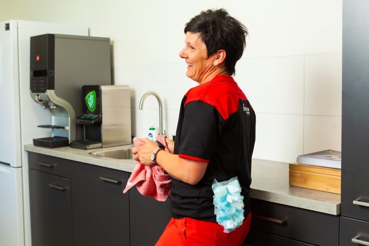 Vrouw lacht tijdens schoonmaken in kantoor keuken.
