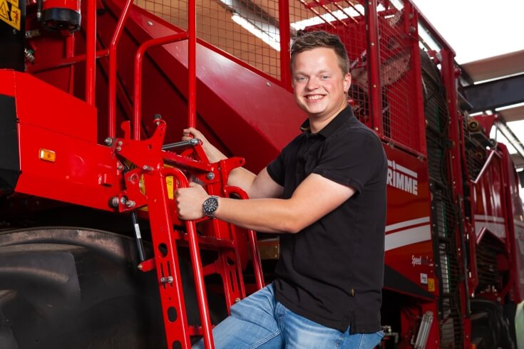 Man poseert bij rode landbouwmachine.
