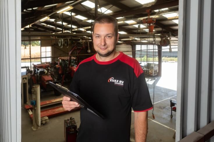 Man met tablet in werkplaats met landbouwmachines.