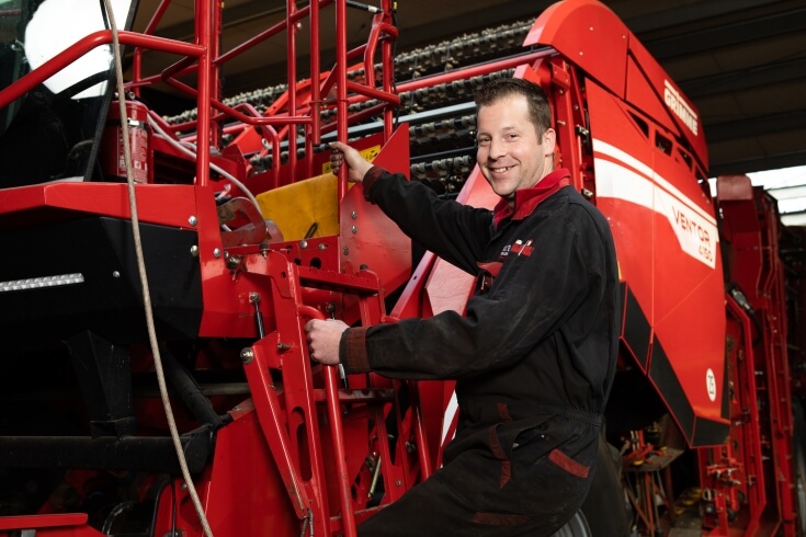 Man op rode landbouwmachine, glimlachend in werkplaats.