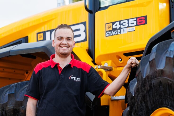 Man bij gele tractor, glimlachend.